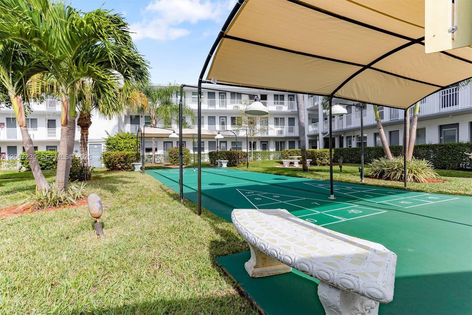 An outdoor shuffleboard court with a canopy sits on a grassy lawn near apartments — 15610 NE 6th Ave # 18C, Miami FL 33162, MIAMI, FL