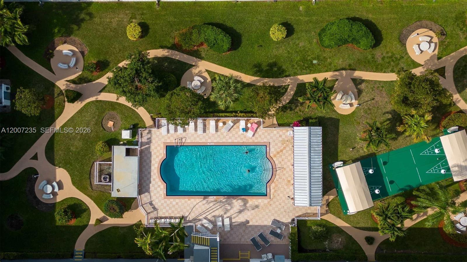 An aerial view shows a swimming pool, shuffleboard court, and walking paths in a landscaped area — 15610 NE 6th Ave # 18C, Miami FL 33162, MIAMI, FL