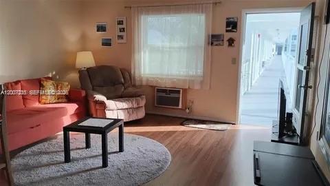 A living room features a pink sofa, a brown armchair, and a door leading outside — 15610 NE 6th Ave # 18C, Miami FL 33162, MIAMI, FL