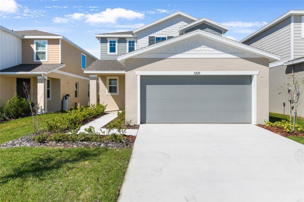 A two-story suburban house features a beige stucco facade, a gray garage door, and landscaping — 5220 BEE BALM STREET, LAKE HAMILTON, FL
