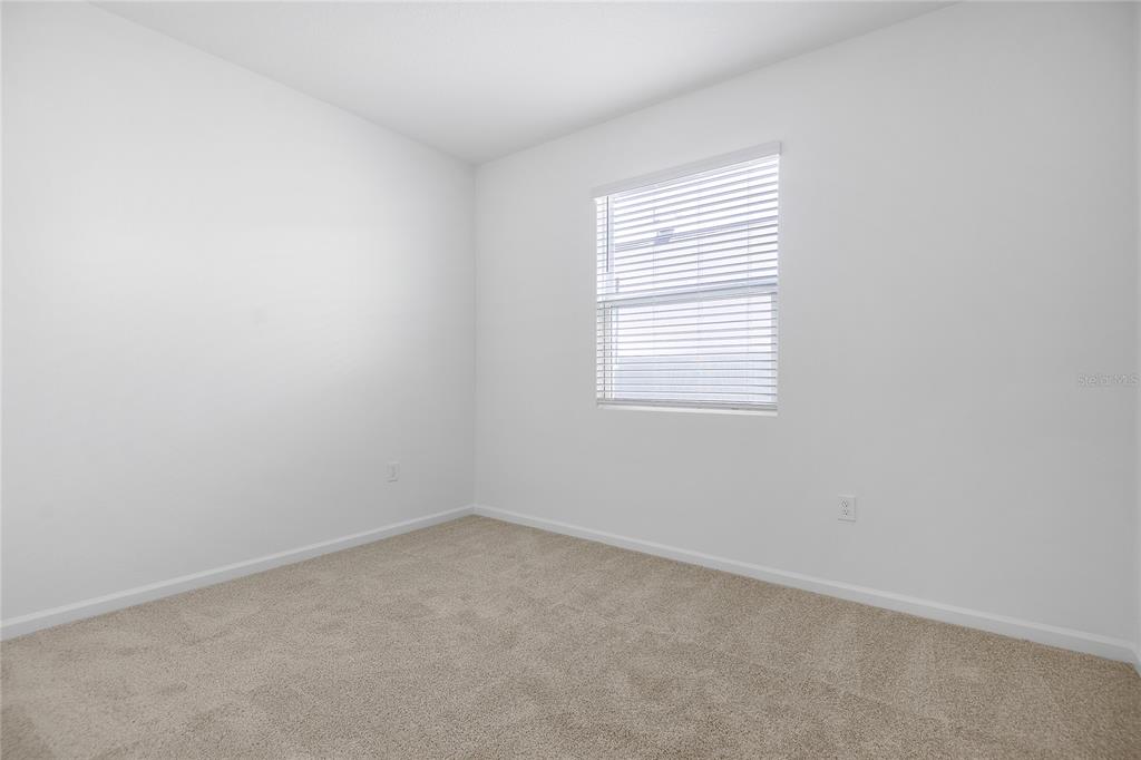 An empty bedroom features white walls, beige carpeting, and a single window with blinds — 5220 BEE BALM STREET, LAKE HAMILTON, FL