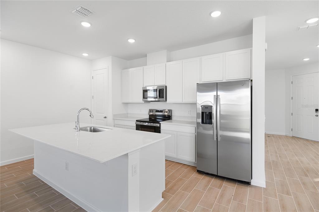 A modern kitchen features white cabinets, stainless steel appliances, a center island, and wood-look flooring — 5220 BEE BALM STREET, LAKE HAMILTON, FL