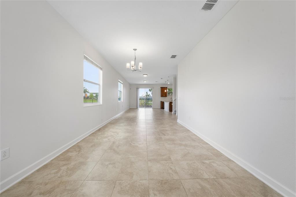 A long, open-concept room with light tile flooring, white walls, and a view of the kitchen — 4756 TRIBUTE TRAIL, KISSIMMEE, FL