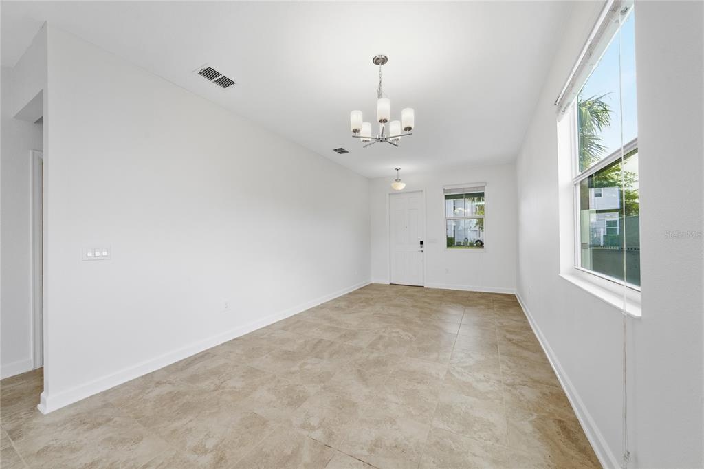 An empty room with beige tile flooring, white walls, a chandelier, and a front door — 4756 TRIBUTE TRAIL, KISSIMMEE, FL