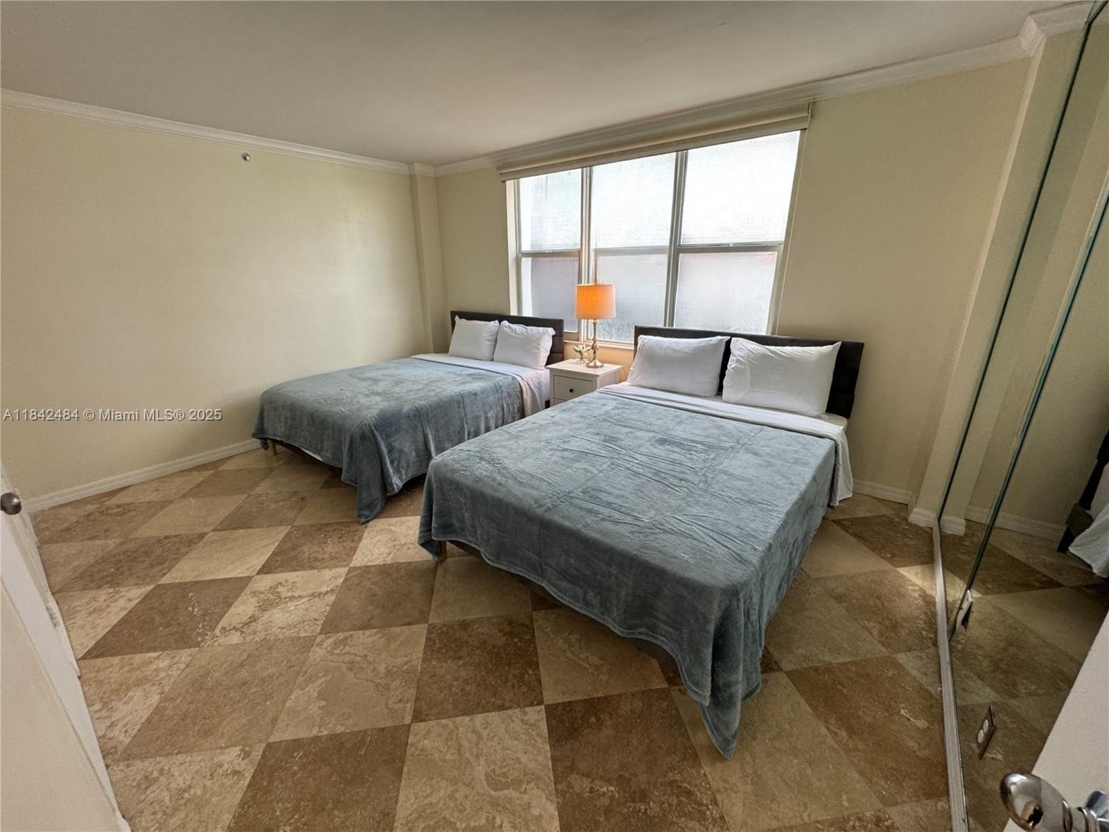 A bedroom features two beds, a nightstand with a lamp, and diamond-patterned tile flooring — 9195 Collins Ave # 912, Surfside FL 33154, SURFSIDE, FL
