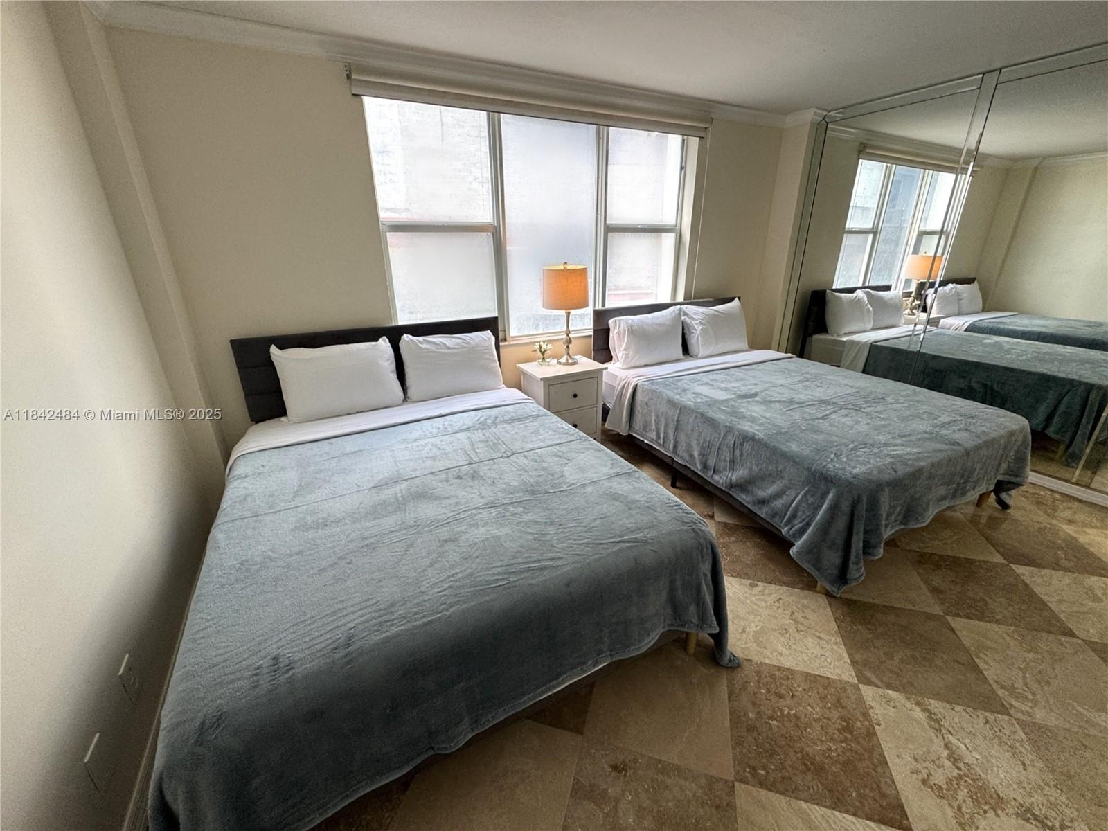 A bedroom features two beds with grey blankets, a nightstand, and a large mirrored wall — 9195 Collins Ave # 912, Surfside FL 33154, SURFSIDE, FL