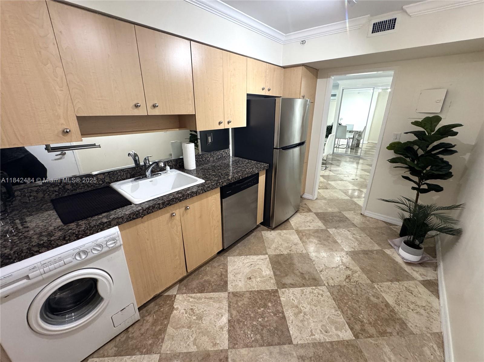 A kitchen features light wood cabinets, granite countertops, a stainless steel refrigerator, and tiled floors — 9195 Collins Ave # 912, Surfside FL 33154, SURFSIDE, FL