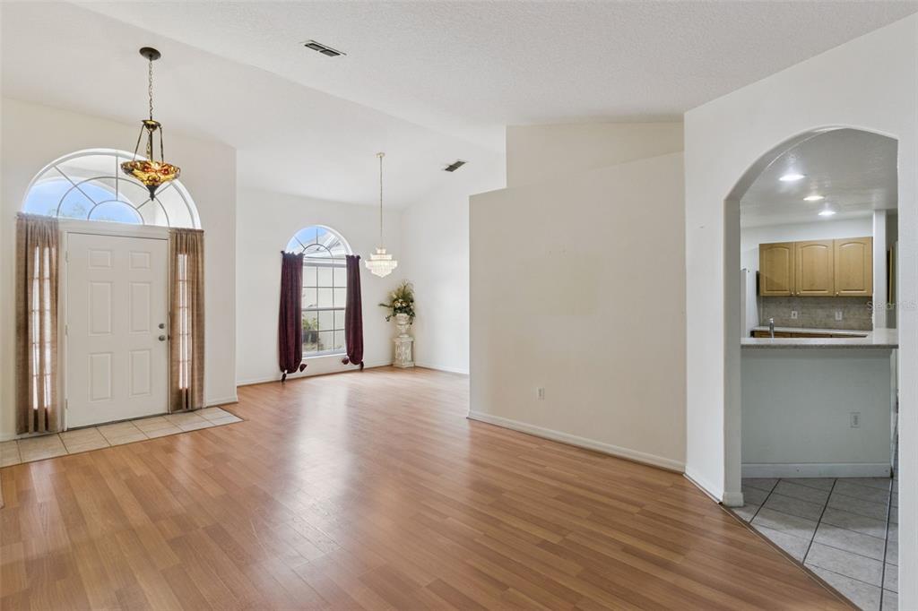 An open living area with wood-look flooring, arched windows, and an adjacent kitchen with cabinets — 236 DOLCETTO DRIVE, DAVENPORT, FL