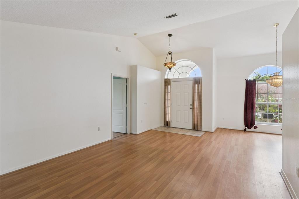 A bright, empty living room features vaulted ceilings, wood-look flooring, and a front entryway door — 236 DOLCETTO DRIVE, DAVENPORT, FL