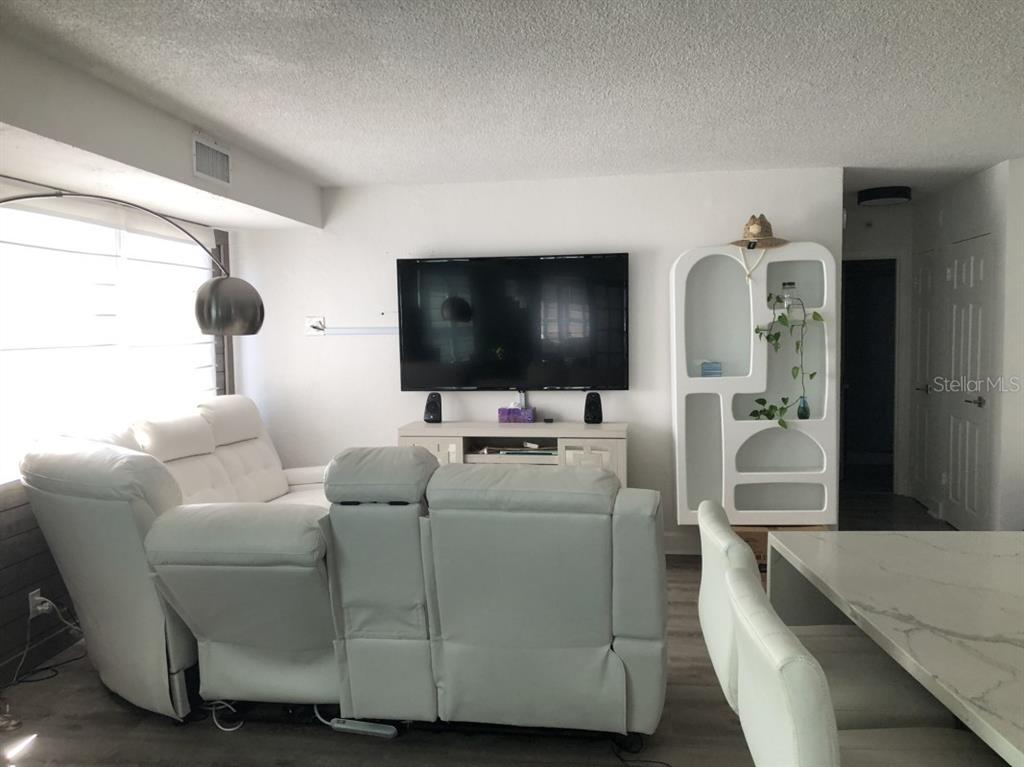 A living room features a white sectional sofa, a wall-mounted television, and a white shelving unit — 3315 58TH AVENUE S UNIT 416, ST PETERSBURG, FL