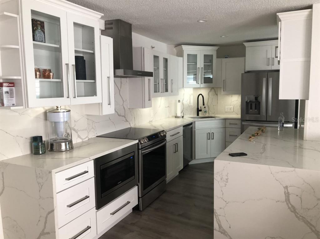 A modern kitchen features white cabinets, marble-patterned countertops, stainless steel appliances, and wood-look flooring — 3315 58TH AVENUE S UNIT 416, ST PETERSBURG, FL