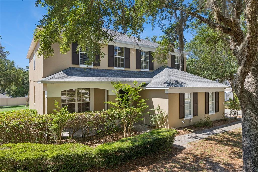 A two-story tan house with dark shutters, a front porch, and mature trees in front — 2692 CEDAR KNOLL DRIVE, APOPKA, FL