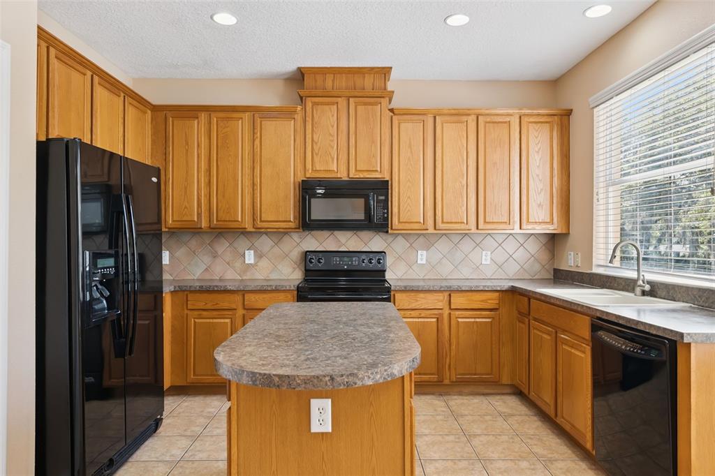A kitchen with oak cabinets, black appliances, a central island, and tile flooring — 2692 CEDAR KNOLL DRIVE, APOPKA, FL