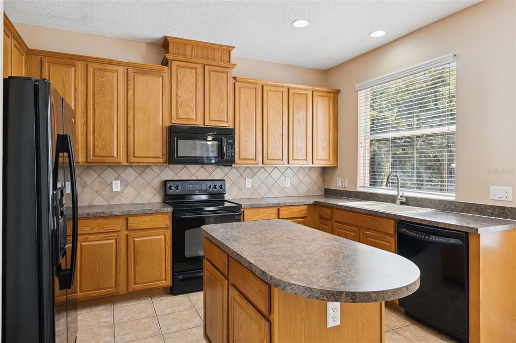 A kitchen with oak cabinets, black appliances, a central island, and a window above the sink — 2692 CEDAR KNOLL DRIVE, APOPKA, FL