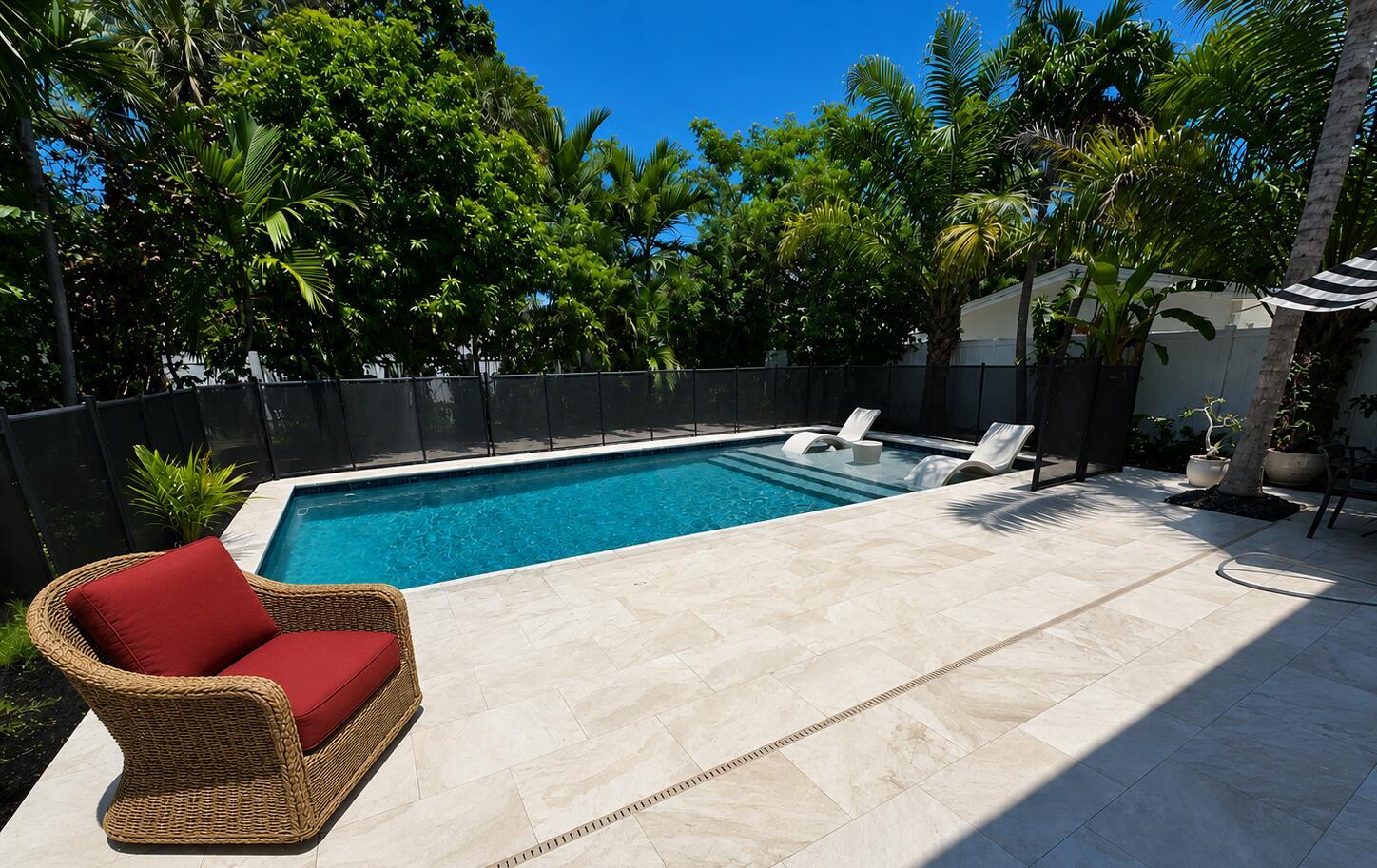 A rectangular swimming pool with a tanning ledge sits on a stone patio with seating — 702 S Atlantic Drive, Lantana FL 33462, LANTANA, FL