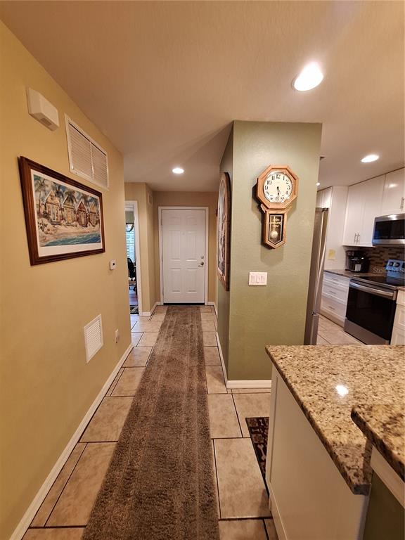 A hallway with tile floors and a runner rug leads to a white front door — 5748 SABAL TRACE DRIVE UNIT 102, NORTH PORT, FL