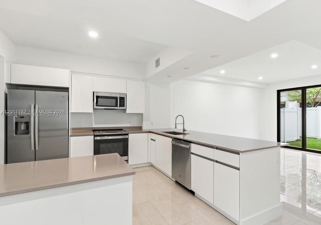 A modern kitchen with white cabinets, stainless steel appliances, and a staircase with black railings — 4130 N Oak Pl # 4130, Dania Beach FL 33314, DANIA BEACH, FL