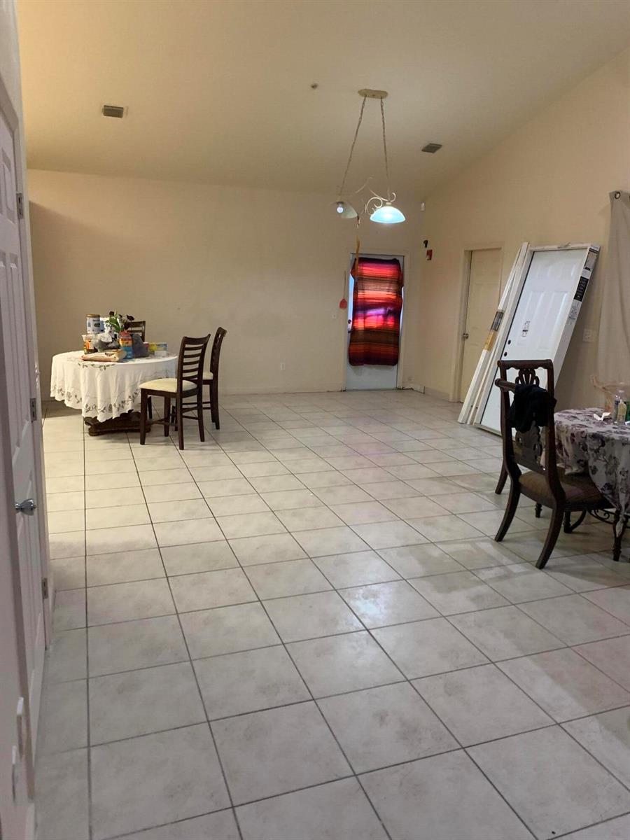 A dining area with tiled floors, two round tables, and a door with a colorful curtain — 198 Sparrow Drive, Royal Palm Beach FL 33411, ROYAL PALM BEACH, FL