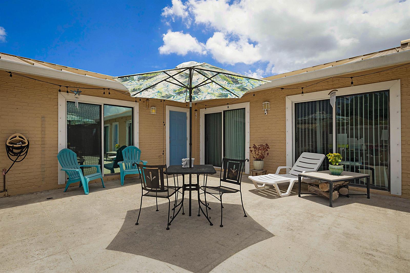 A patio with a table, chairs, lounge chair, and umbrella against a tan brick house — 5729 Golden Eagle Circle, Palm Beach Gardens FL 33418, PALM BEACH GARDENS, FL
