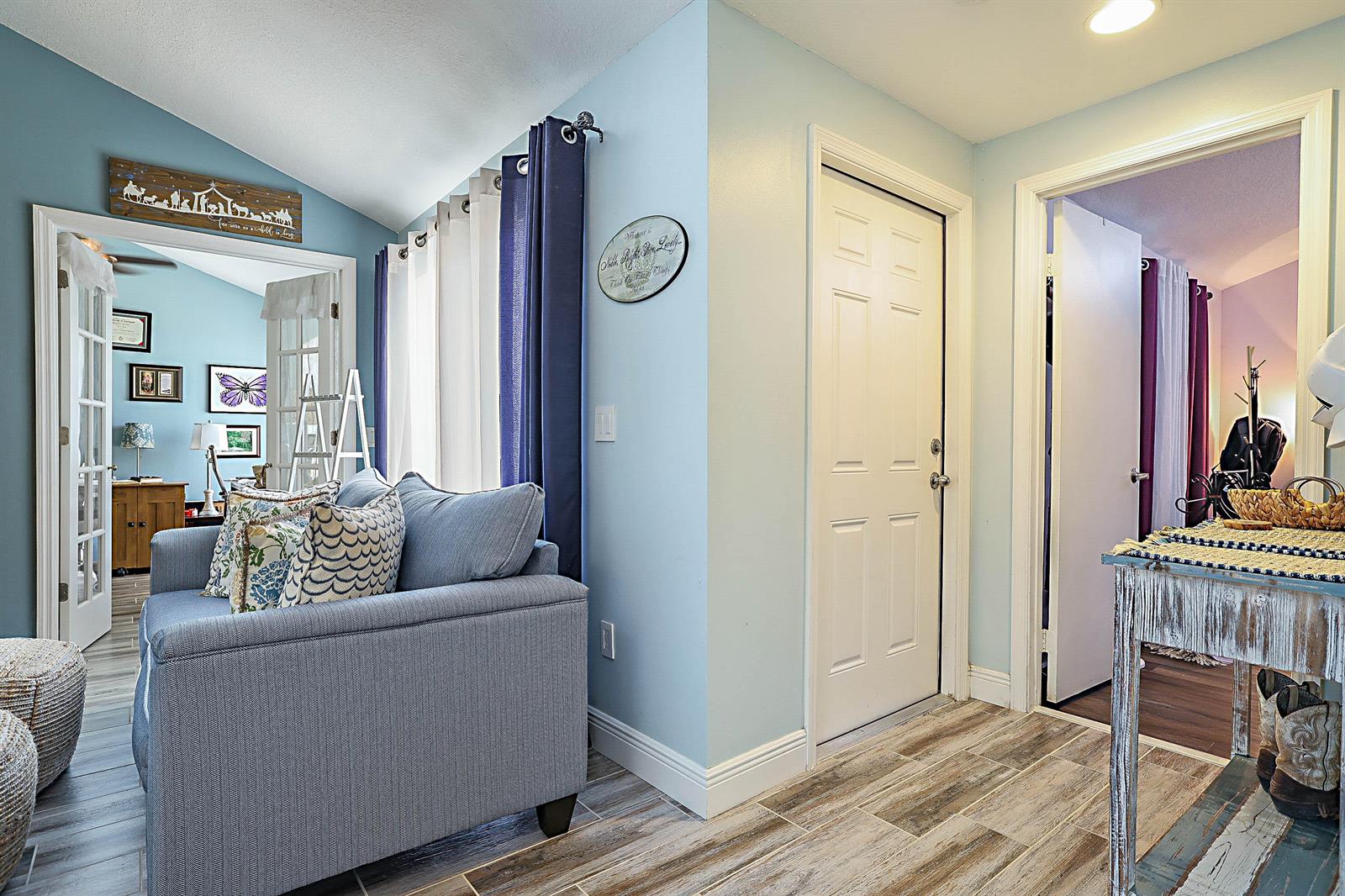A living room with light blue walls, a blue sofa, and wood-look tile flooring — 5729 Golden Eagle Circle, Palm Beach Gardens FL 33418, PALM BEACH GARDENS, FL