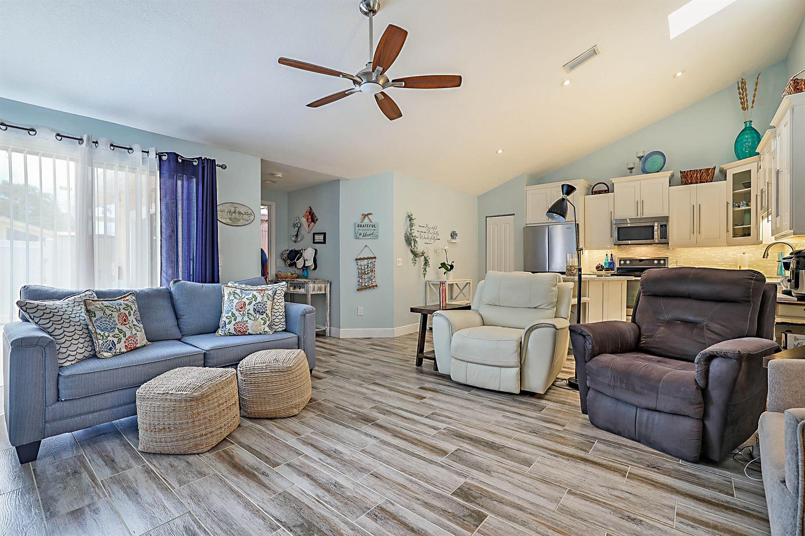 A living room with wood-look tile floors, a blue sofa, and an open-concept kitchen — 5729 Golden Eagle Circle, Palm Beach Gardens FL 33418, PALM BEACH GARDENS, FL