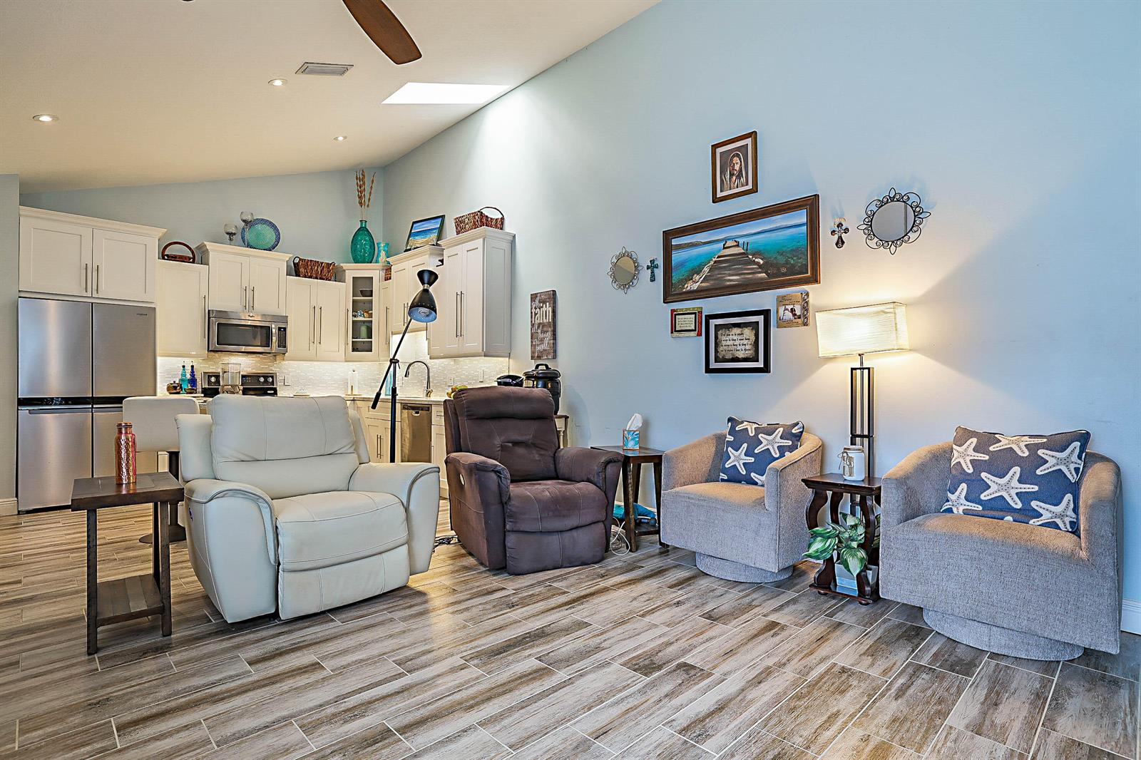 A living room with four chairs and a kitchen area featuring white cabinets and stainless appliances — 5729 Golden Eagle Circle, Palm Beach Gardens FL 33418, PALM BEACH GARDENS, FL