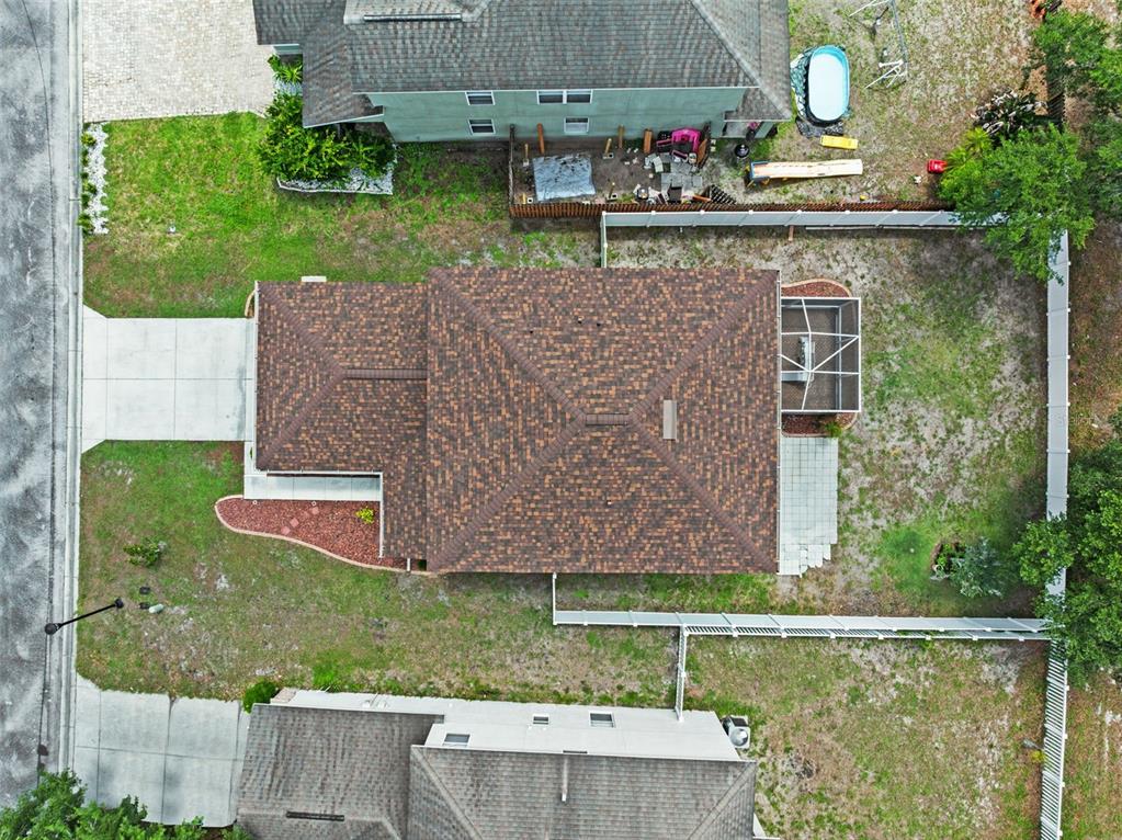 An aerial view shows a house with a brown shingled roof, a screened patio, and a fenced backyard — 12607 CHENWOOD AVENUE, HUDSON, FL