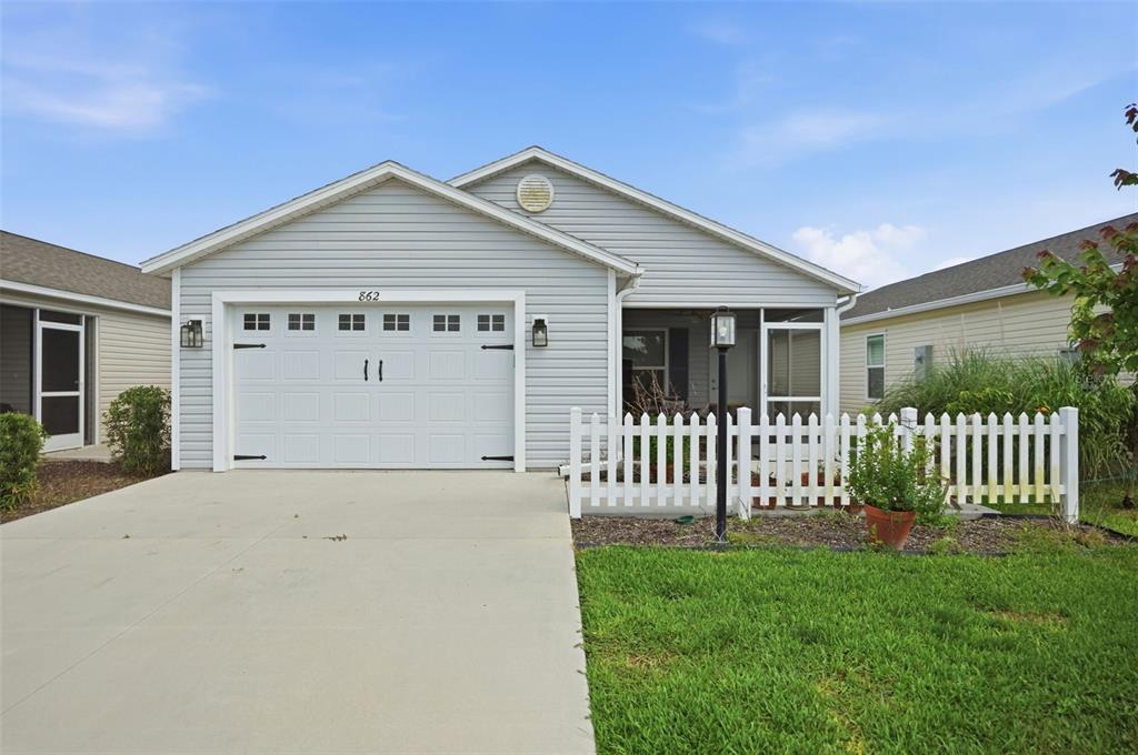 A single-story house with light gray siding, a white garage door, and a front porch — 862 SPRING AVENUE, THE VILLAGES, FL