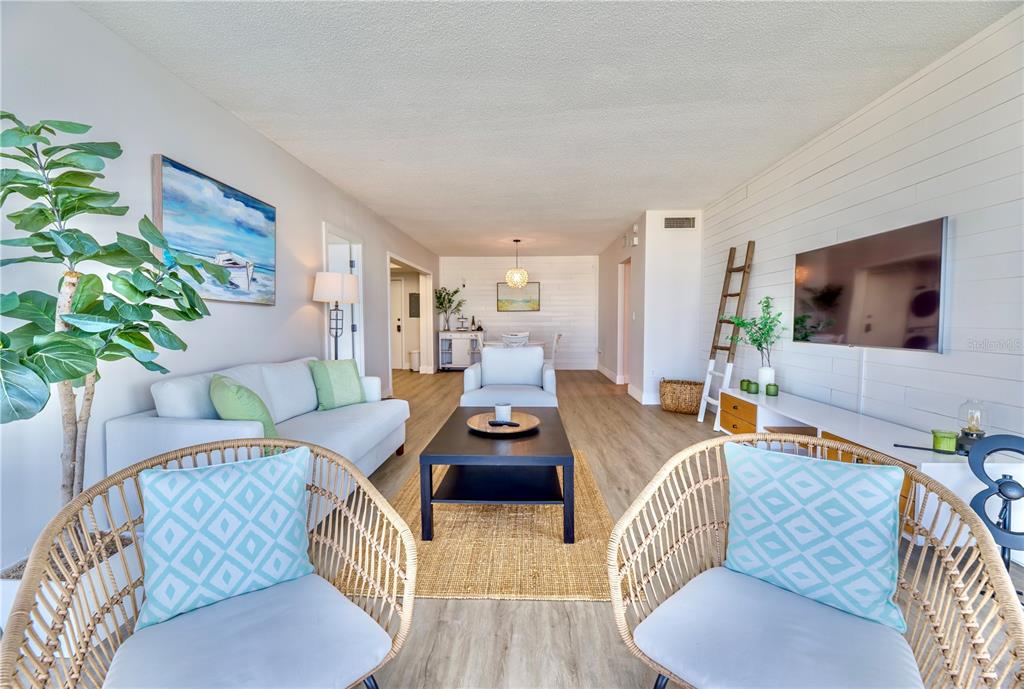 A living room features light wood flooring, a white shiplap wall, and wicker accent chairs — 100 PIERCE STREET UNIT 1102, CLEARWATER, FL