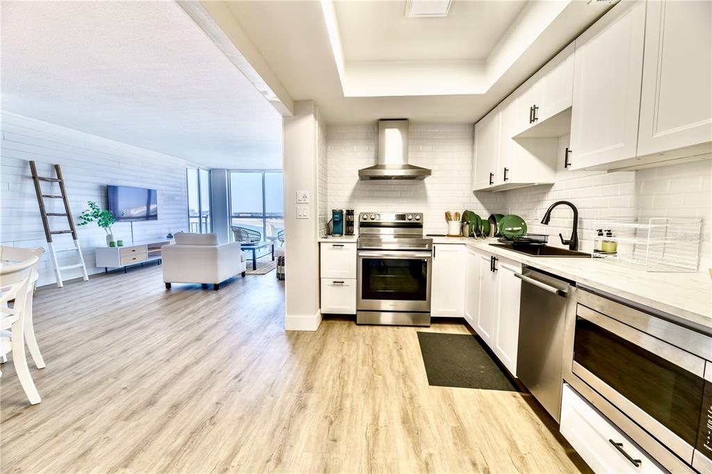 A modern kitchen with white cabinets and stainless steel appliances opens into a living area — 100 PIERCE STREET UNIT 1102, CLEARWATER, FL