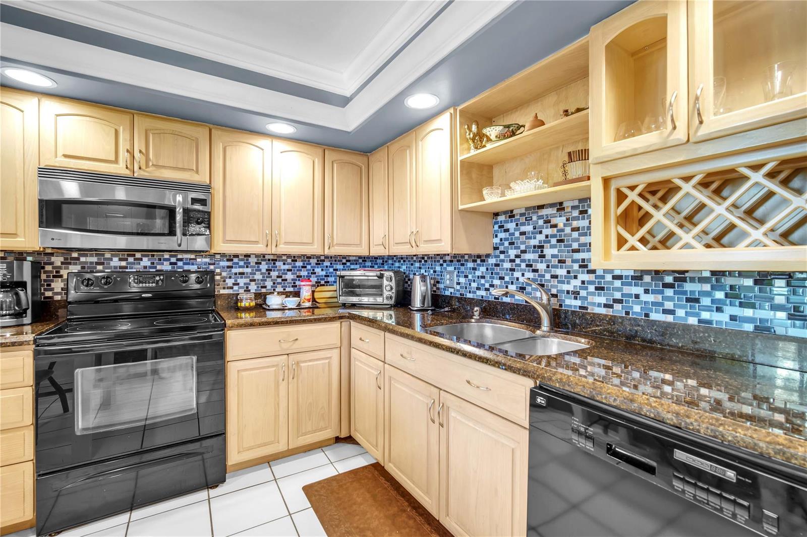 A kitchen with light wood cabinets, dark granite countertops, and a blue mosaic tile backsplash — 400 Oaks Lane # 115, Pompano Beach FL 33069, POMPANO BEACH, FL