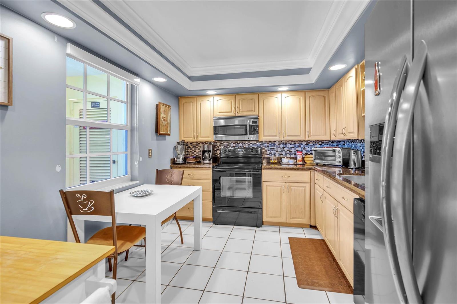 A kitchen with light wood cabinets, black appliances, a white dining table, and tiled floors — 400 Oaks Lane # 115, Pompano Beach FL 33069, POMPANO BEACH, FL