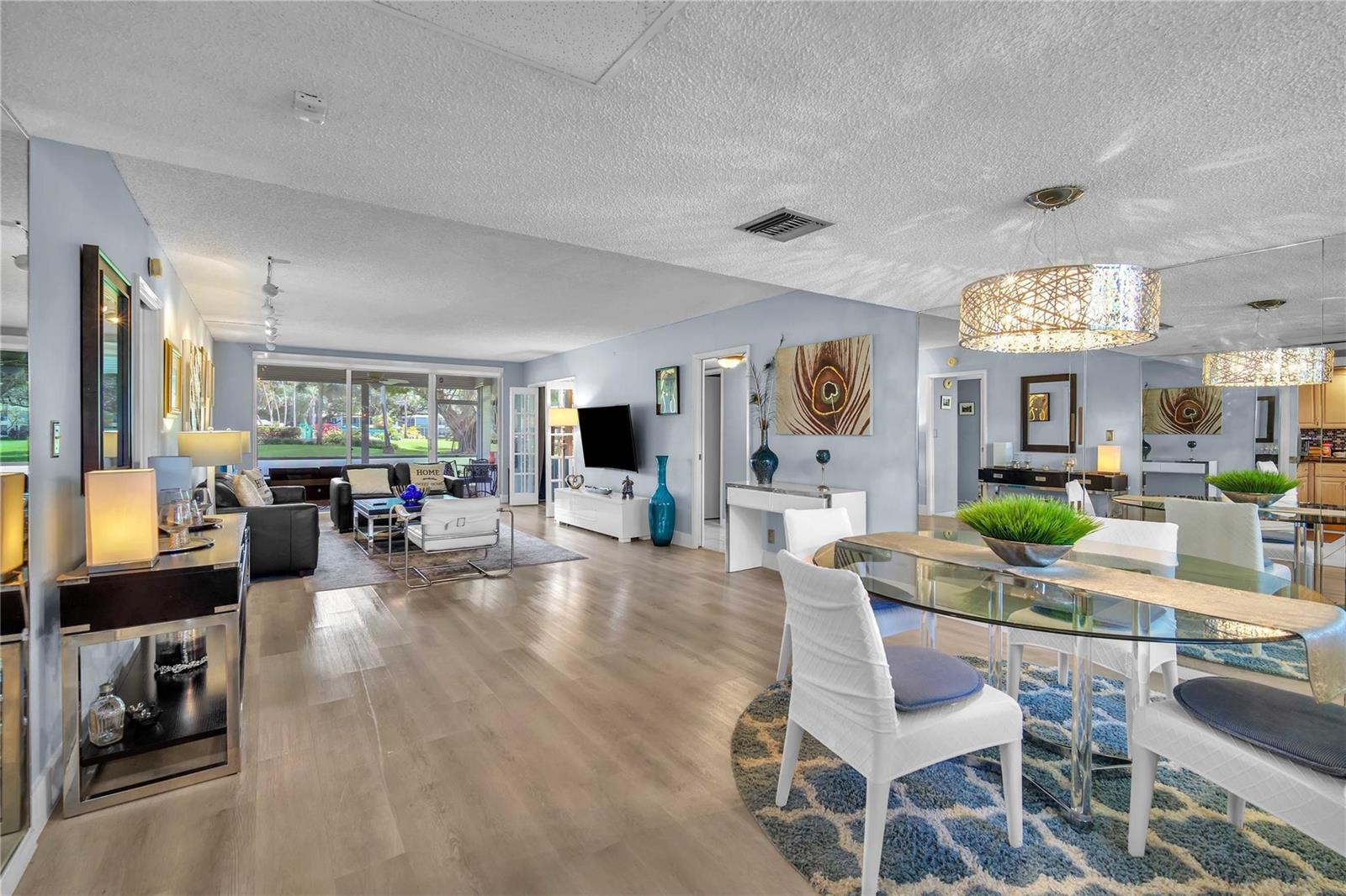 An open-concept living and dining area features light wood flooring, a glass table, and sliding doors — 400 Oaks Lane # 115, Pompano Beach FL 33069, POMPANO BEACH, FL