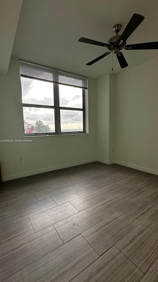 An empty room features light wood-look tile flooring, a ceiling fan, and a large window — 1776 Polk St # 1403, Hollywood FL 33020, HOLLYWOOD, FL