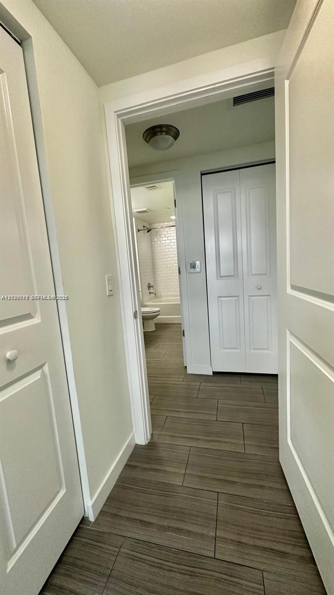 A hallway with wood-look tile flooring leads to a bathroom with a white vanity — 1776 Polk St # 1403, Hollywood FL 33020, HOLLYWOOD, FL