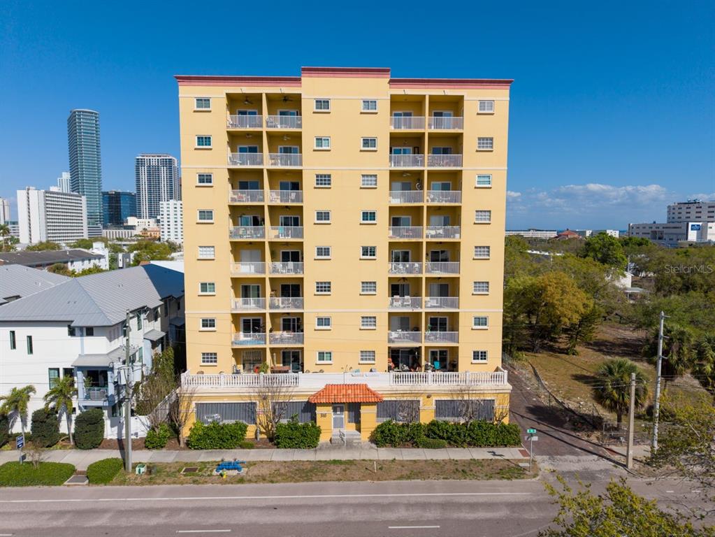 A multi-story yellow apartment building stands under a clear blue sky — 316 8TH STREET S UNIT 402, ST PETERSBURG, FL