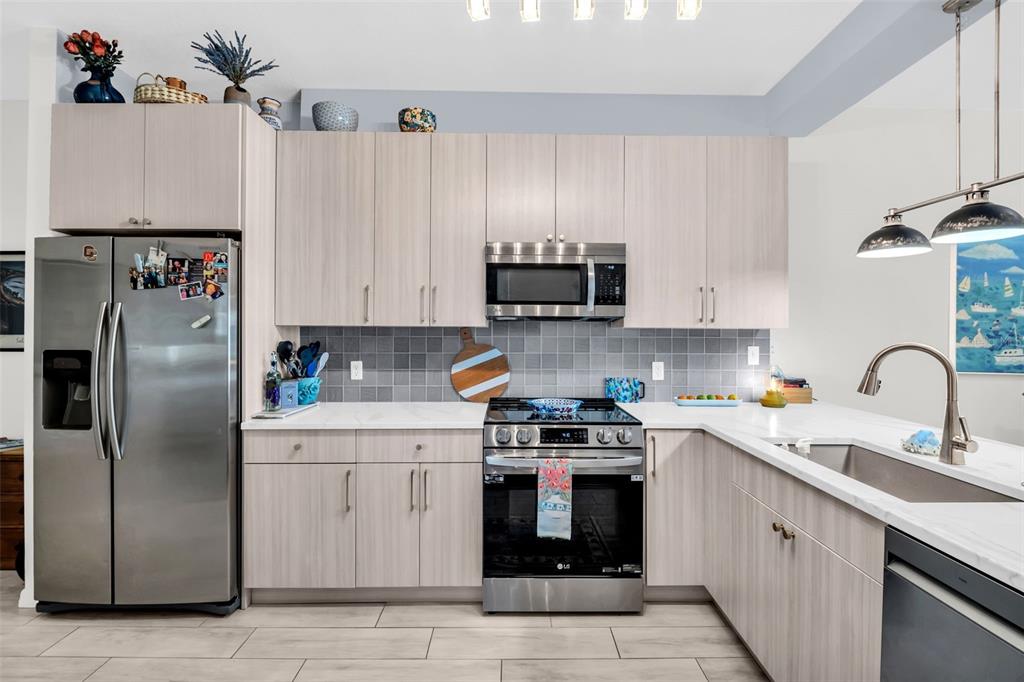A modern kitchen features light wood cabinets, stainless steel appliances, and a gray tiled backsplash — 316 8TH STREET S UNIT 402, ST PETERSBURG, FL