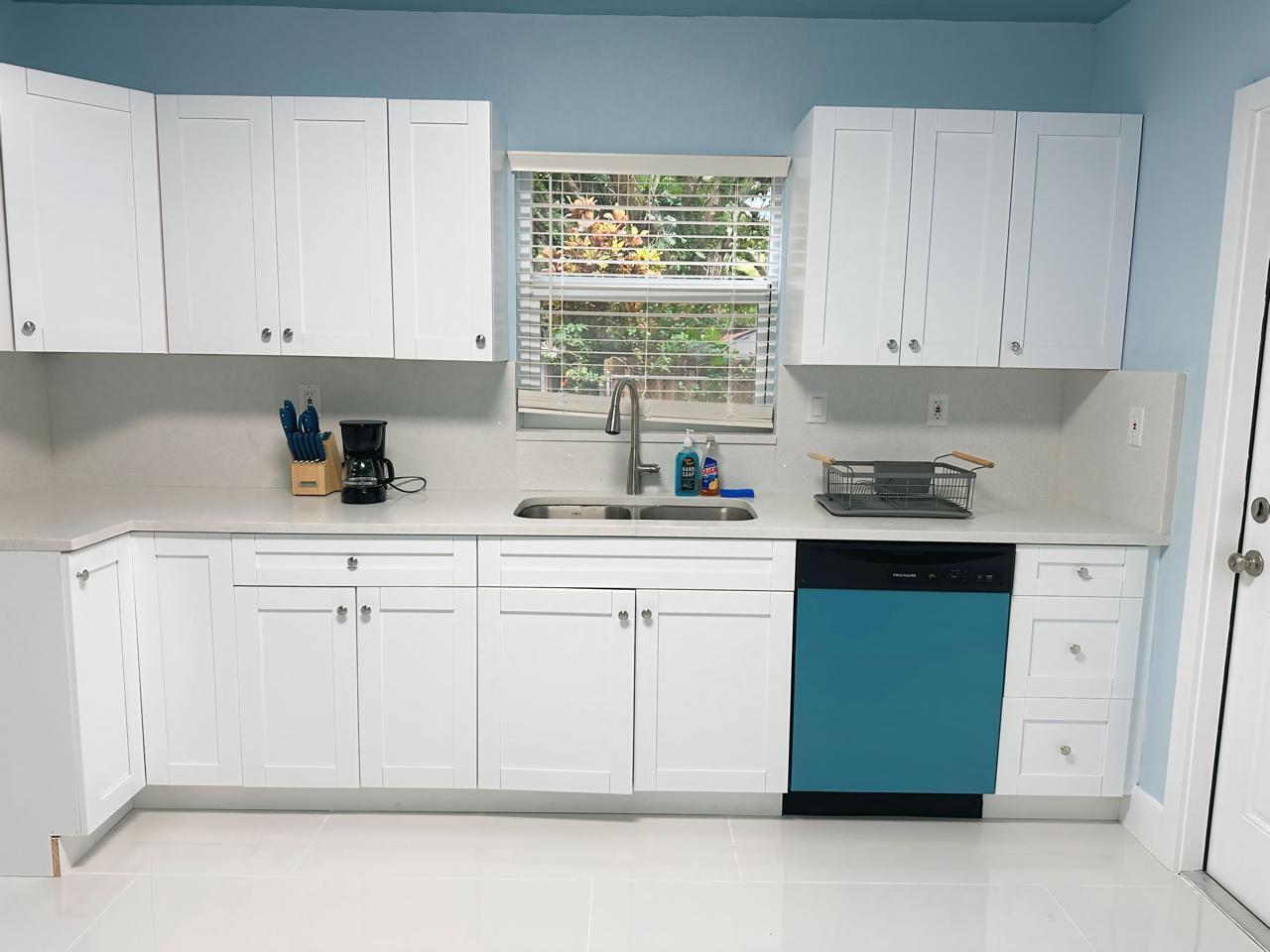 A kitchen features white shaker cabinets, light countertops, a teal dishwasher, and blue wall paint — 1702 NE 146th Street, Miami FL 33181, MIAMI, FL