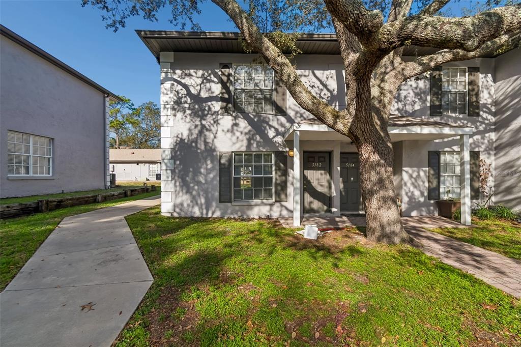 A two-story residential building with gray stucco walls, dark shutters, and a large oak tree — 5182 SUNRIDGE PALMS DRIVE UNIT 5182, TAMPA, FL