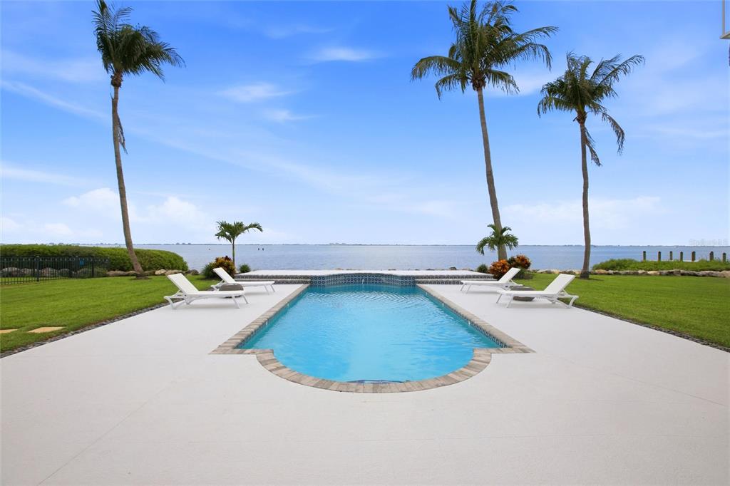 A swimming pool sits on a patio overlooking a large body of water with palm trees — 7524 WESTMORELAND DRIVE, SARASOTA, FL