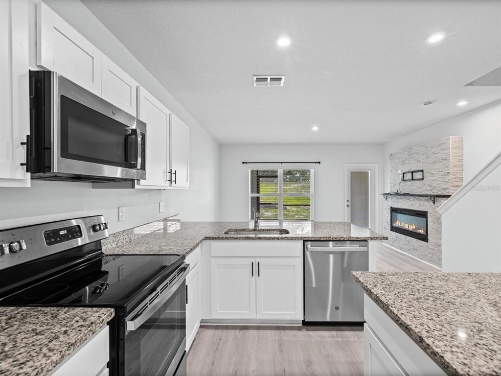 A kitchen with white cabinets, granite countertops, stainless steel appliances, and a fireplace in view — 3154 VICTORIA INLET DRIVE, HOLIDAY, FL