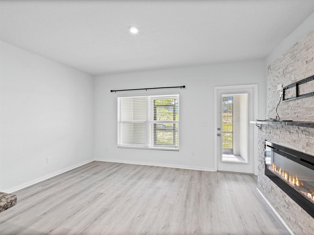 A living room features light wood-look flooring, white walls, a stone fireplace, and a door — 3154 VICTORIA INLET DRIVE, HOLIDAY, FL