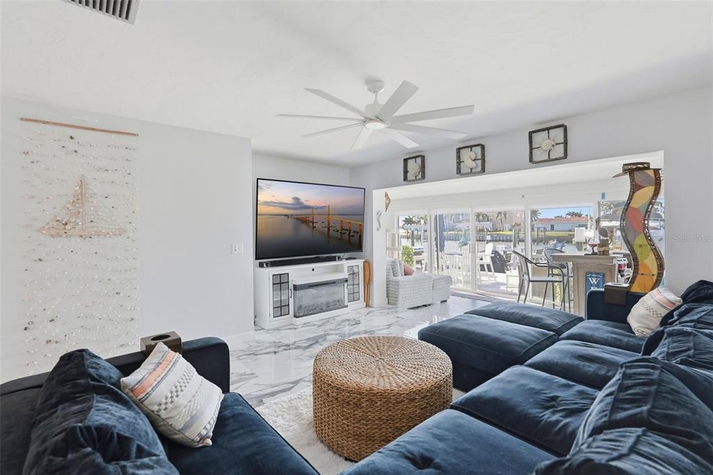 A living room features a blue sectional sofa, a television, and sliding doors overlooking water — 573 BOCA CIEGA POINT BOULEVARD N, ST PETERSBURG, FL