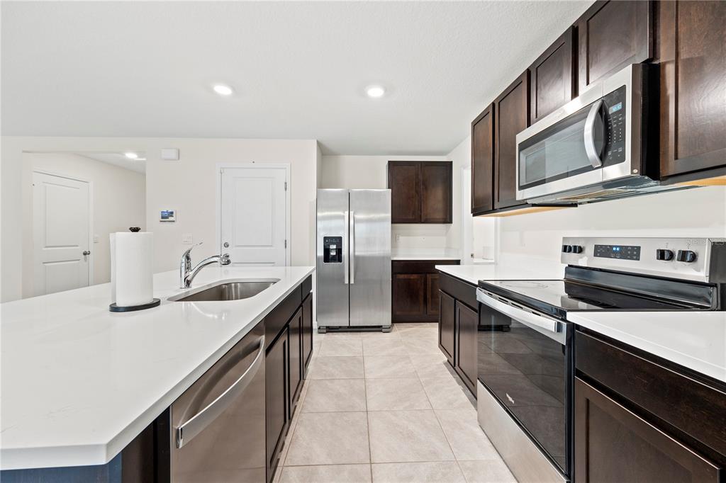 A kitchen features dark wood cabinets, stainless steel appliances, and a white quartz island countertop — 24595 NW 11TH PLACE, NEWBERRY, FL