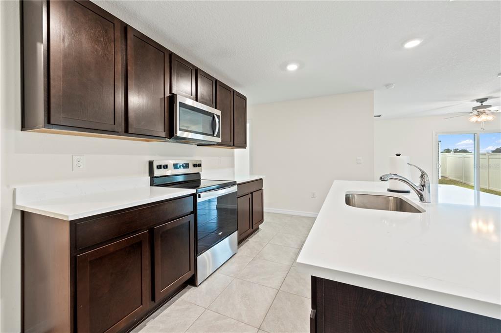 A kitchen features dark wood cabinets, white countertops, stainless steel appliances, and light tile flooring — 24595 NW 11TH PLACE, NEWBERRY, FL