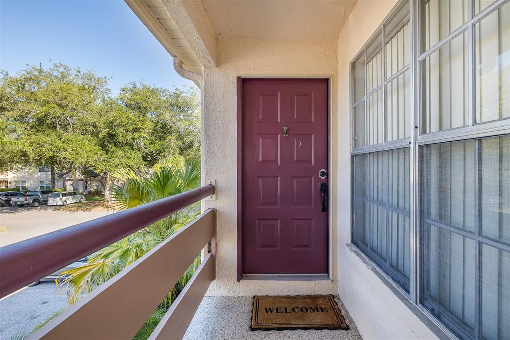 A purple front door with a welcome mat on a covered balcony overlooking a parking lot — 7900 HARDWICK DRIVE UNIT 827, NEW PORT RICHEY, FL