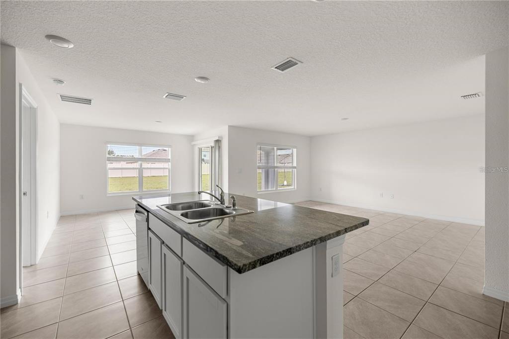 A kitchen island with a granite countertop sits in an open-concept room with tile flooring — 8904 SW 50TH TERRACE, OCALA, FL