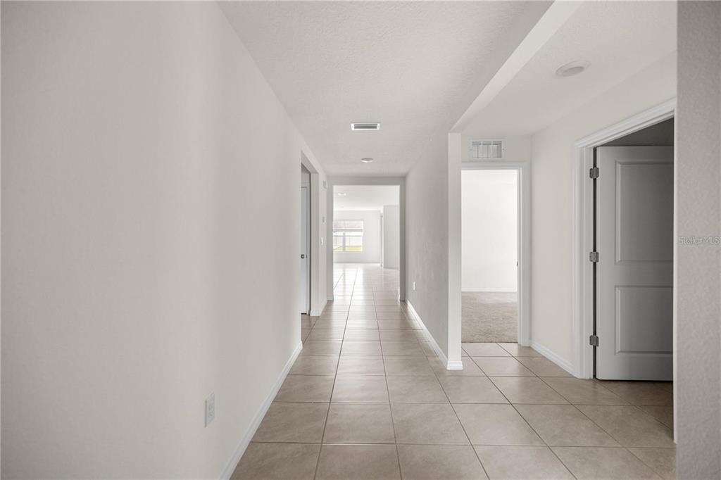 A hallway with light-colored tile flooring leads toward an open living area with a window — 8904 SW 50TH TERRACE, OCALA, FL