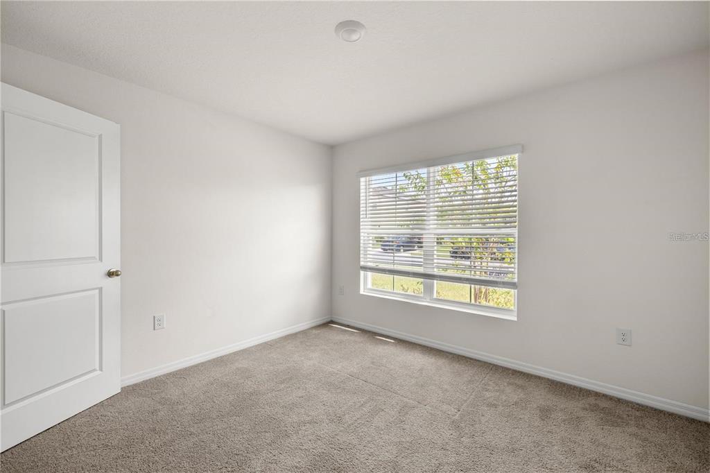 An empty bedroom features white walls, gray carpet, a single window with blinds, and a door — 8904 SW 50TH TERRACE, OCALA, FL