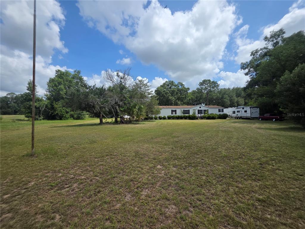A wide, grassy yard leads to a single-story home with an attached recreational vehicle — 8095 SE 131ST PLACE, SUMMERFIELD, FL